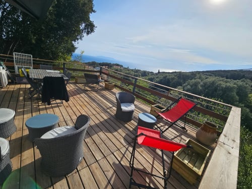 Terrasse en bois à la villa Altezza à Brando avec vue sur mer, mobilier de jardin, transats et paysage forestier