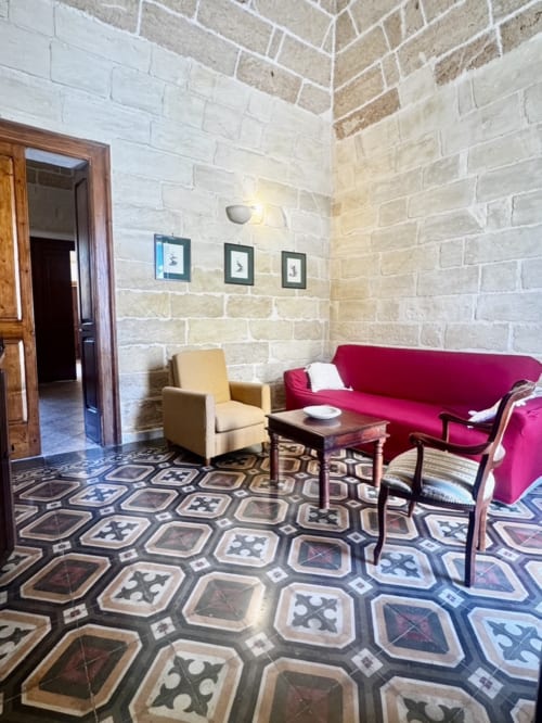 Elegant lounge at HABITARE Lecce with red sofa, cream chair, patterned tile floor, and exposed stone walls