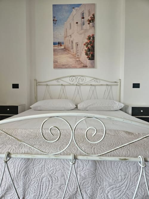 Camera elegante al B&B Hélios di Nardò con letto in ferro battuto, biancheria bianca e arte costiera italiana sopra