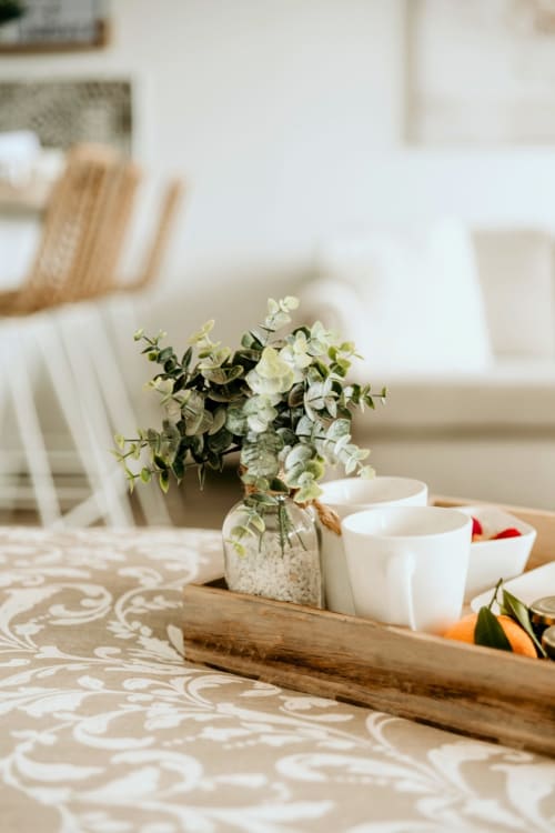 Elegant table setting at Sable & Pampas with white flowers, green eucalyptus, ceramic cups, and patterned beige tablecloth