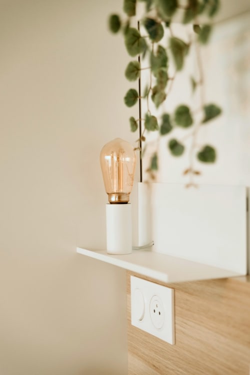 Minimalist bedside lamp with amber bulb beside potted plant at Sable & Pampas, Carnon-Plage