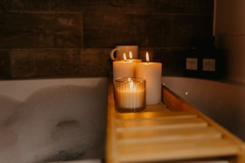 Luxurious spa setting at Sable & Pampas with lit candles on wooden tub caddy overlooking bathtub in Carnon-Plage