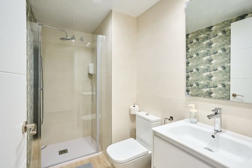 Baño moderno en Tr3sor Homes Calella con ducha de cristal, lavabo blanco, inodoro y pared de azulejos decorativos