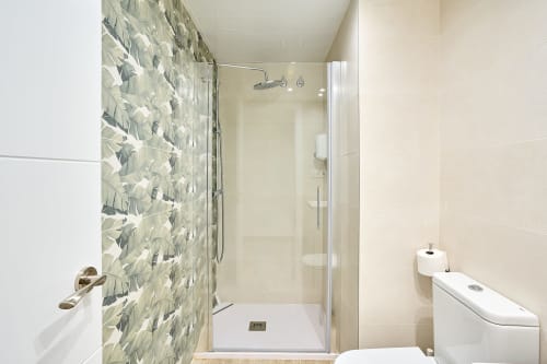Baño moderno con ducha de azulejos geométricos y mamparas de cristal en apartamento Tr3sor Homes, Calella