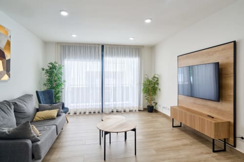 Salón moderno del apartamento Tr3sor 11 en Calella con sofá gris, mueble televisión en madera, plantas y luz natural