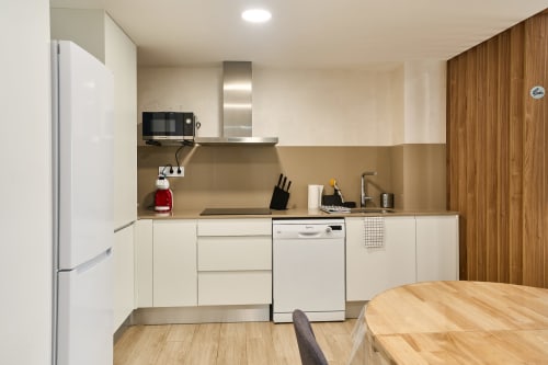 Cocina moderna en apartamento Tr3sor 11, Calella, con muebles blancos, electrodomésticos de acero inoxidable y detalles de madera.