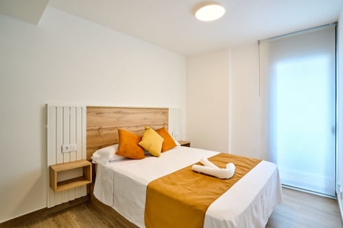 Dormitorio moderno en Tr3sor Homes Calella con cabecero de madera, almohadas naranjas y puertas de cristal correderas