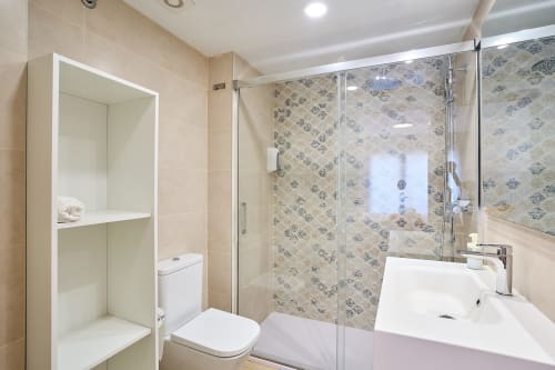 Baño moderno en apartamento Tr3sor 11 en Calella con ducha de cristal, lavabo blanco y paredes con azulejos estampados