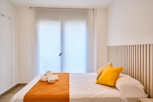 Dormitorio moderno en Tr3sor Homes, Calella, con cama doble, almohada amarilla, puertas con vistas al mar y radiador