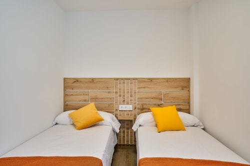 Dormitorio doble en apartamento Tr3sor Homes en Calella con cabecero de madera, almohadas amarillas y ropa de cama blanca