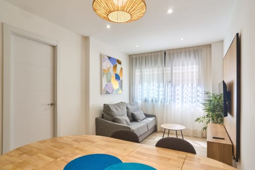 Sala de estar moderna de planta abierta con suelos de madera, sofá gris, TV y amplia luz natural en Tr3sor Homes