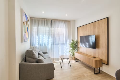 Moderno salón del apartamento Tr3sor B2 en Calella con sofá gris, pared de TV en madera, televisor de pantalla plana y luz natural