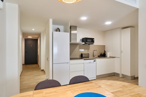 Cocina y comedor moderno en apartamento Tr3sor B2, Calella con muebles blancos, electrodomésticos de acero inoxidable y madera