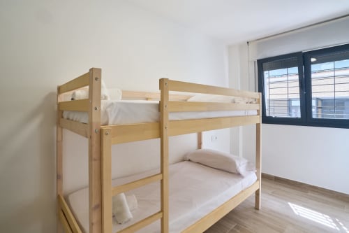Litera de madera con ropa de cama blanca en habitación luminosa con ventanales en Tr3sor Homes, Calella
