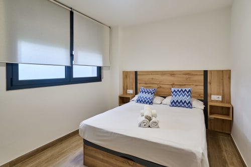 Dormitorio moderno en Tr3sor Homes Calella con cama de madera, almohadas azules chevron, toallas enrolladas y marco oscuro