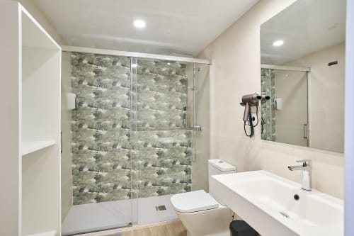 Baño moderno con ducha a ras de suelo, azulejos con patrón, lavabo blanco y espejo del apartamento Tr3sor Homes en Calella