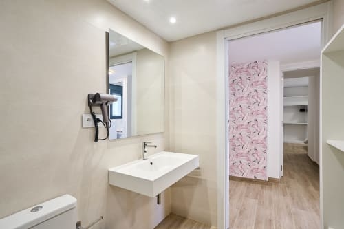 Baño moderno en apartamento Tr3sor Homes, Calella: lavabo blanco, espejo, secador y puerta estampada rosa hacia vestidor
