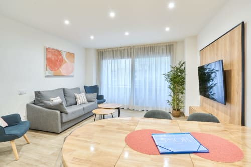 Sala moderna del apartamento Tr3sor 12 en Calella, con sofá gris, pared de TV en madera y diseño abierto con luz natural