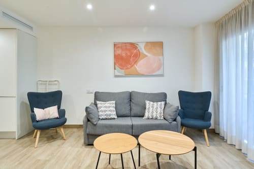Moderna sala de estar en apartamento Tr3sor Homes, Calella: sofá gris, sillones azules, mesas de madera y arte mural cítrico