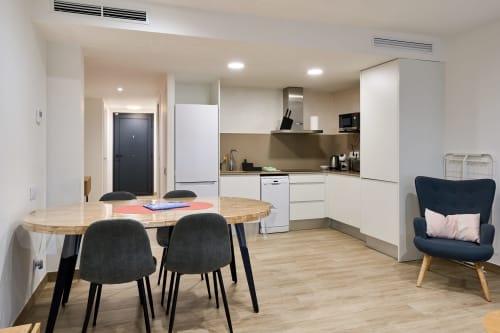 Cocina abierta y comedor moderno en apartamento Tr3sor Homes de Calella con mesa de madera, sillas negras y tonos azul marino