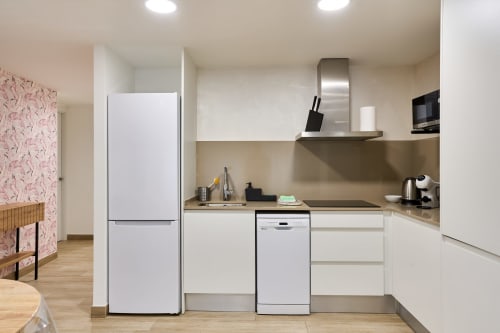 Cocina moderna en apartamento Tr3sor Homes de Calella con electrodomésticos blancos, campana acero inoxidable y zona de comedor.