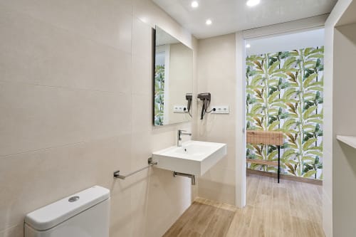 Baño moderno del apartamento Tr3sor Homes en Calella con lavabo blanco, espejo, inodoro y acceso a patio con plantas tropicales