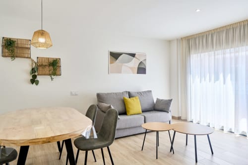Salón moderno en apartamento Tr3sor Homes, Calella con sofá gris, mesa de madera y luz natural abundante