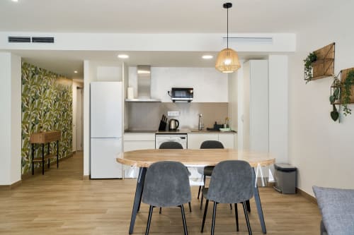 Cocina abierta y comedor moderno en apartamento Tr3sor 13, Calella, con mesa de madera, sillas grises y muebles blancos