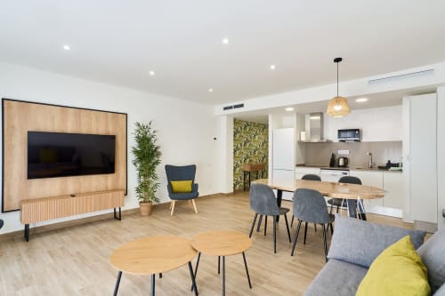 Zona de estar moderna y diáfana en apartamento Tr3sor 13 de Calella con cocina, mesa de comedor, TV en pared de madera y