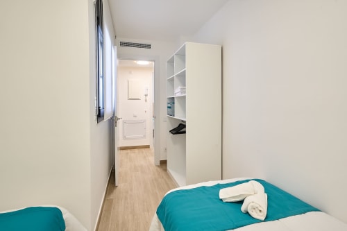 Dormitorio en apartamento Tr3sor Homes de Calella con camas gemelas, estantes blancos y acceso a baño privado