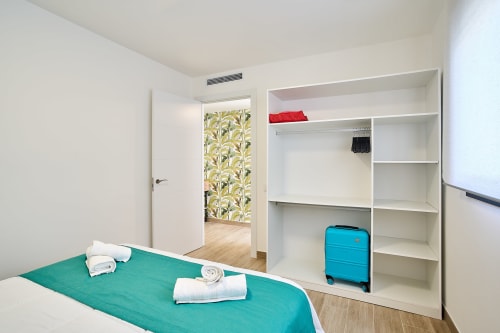 Dormitorio de Tr3sor Homes en Calella con cama turquesa, estantería blanca, maleta azul y acceso al baño