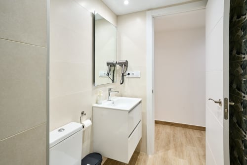 Baño moderno en apartamento Tr3sor 21, Calella, con tocador blanco, espejo, inodoro y ducha con azulejos
