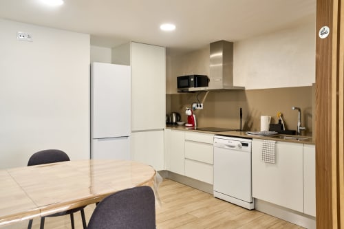 Cocina moderna con comedor en apartamento Tr3sor 21, Calella. Mobiliario blanco, lavavajillas, microondas y refrigerador.