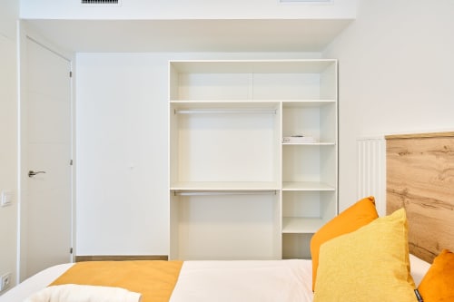 Dormitorio moderno en apartamento Tr3sor 21 de Calella con armario empotrado blanco, cama de madera y almohadas amarillas