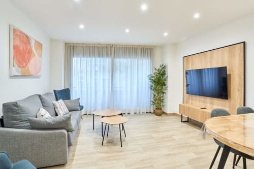Sala de estar moderna en apartamento Tr3sor 22, Calella, con sofás grises, mueble TV en madera, comedor y amplias ventanas