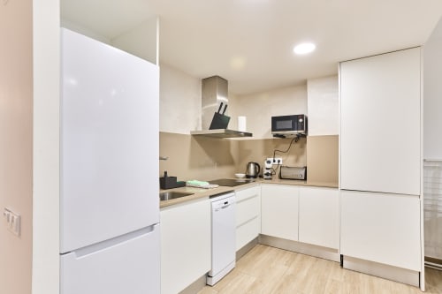Cocina moderna en apartamento Tr3sor 22, Calella con muebles blancos, salpicadero beige, electrodomésticos acero inoxidable y