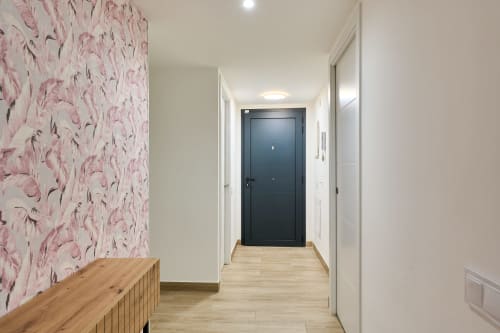 Pasillo moderno en apartamento Tr3sor Homes, Calella con papel pintado floral, suelos de madera y puerta de entrada oscura