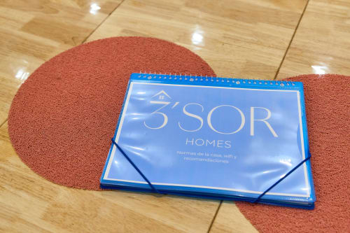 Folleto de bienvenida de Tr3sor Homes en piso de madera con tapete circular rojo en Calella