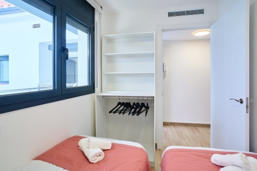 Dormitorio moderno en Tr3sor Homes, Calella, con dos camas, armario empotrado con perchas, estantes y acceso a baño privado