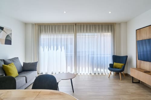 Elegante sala de estar en apartamento Tr3sor Homes, Calella: sofá gris, detalles amarillos, sillón y ventanales