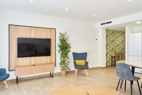 Moderna sala de estar en Tr3sor Homes, Calella: TV mural, sillas azules, suelos de madera y diseño contemporáneo