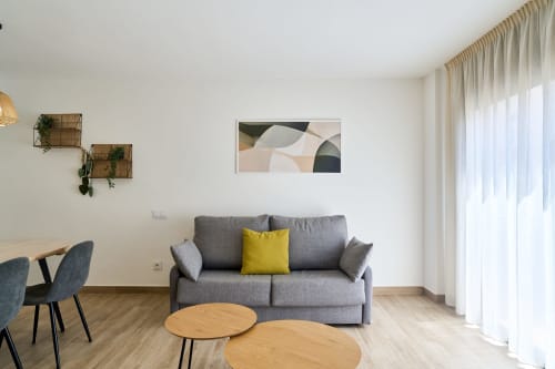Sala moderna en apartamento de Calella con sofá gris, mesas de madera y luz natural en Tr3sor Homes