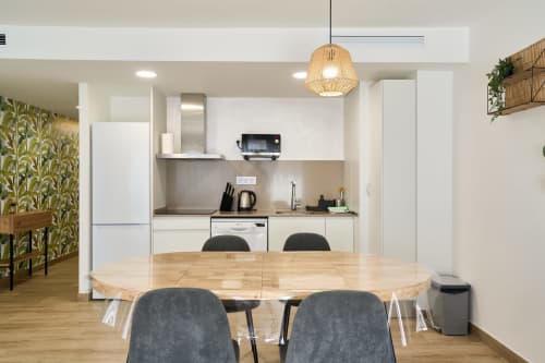 Cocina y comedor modernos en apartamento Tr3sor Homes, Calella con mesa de madera, muebles blancos e iluminación colgante