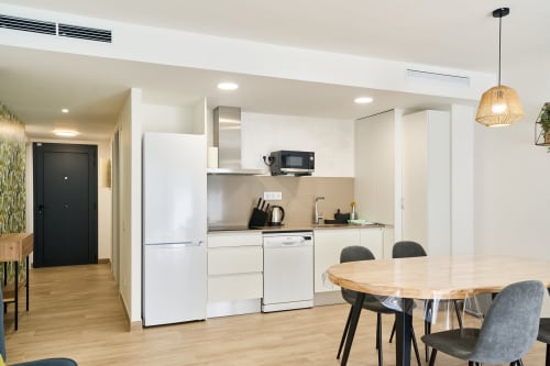 Cocina y comedor modernos en el apartamento Tr3sor 23 de Calella con muebles blancos, mesa de madera y asientos contemporáneos.