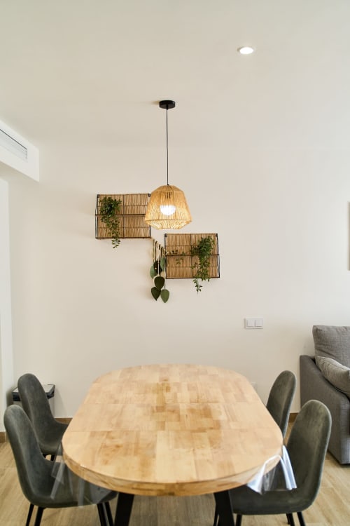 Comedor moderno en apartamento Tr3sor 23, Calella con mesa de madera, sillas grises, lámpara colgante de ratán y maceteros de pared