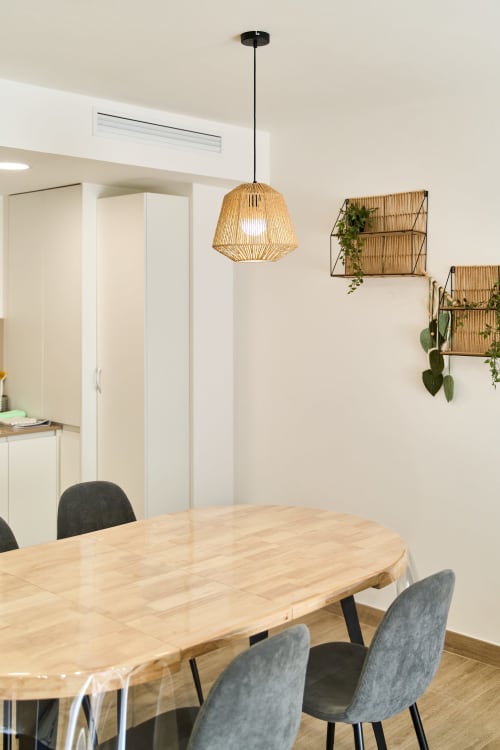Área de comedor moderna en apartamento Tr3sor Homes con mesa de madera, sillas grises y lámpara colgante tejida.