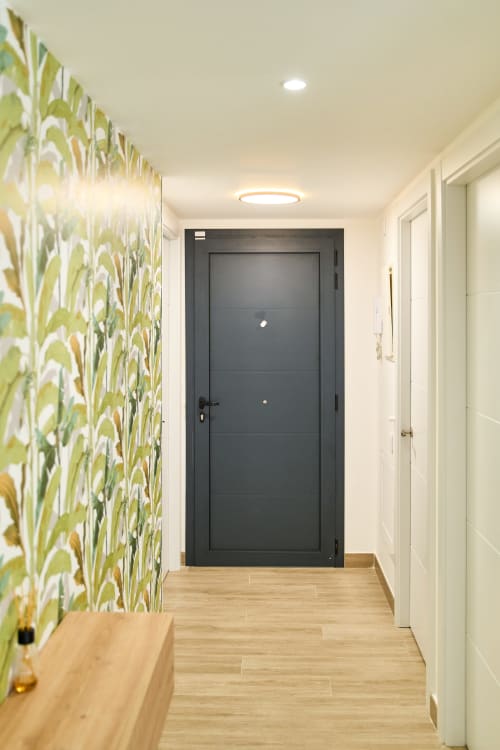 Pasillo moderno en apartamento Tr3sor 23, Calella, con papel tapiz botánico, puerta de entrada oscura y piso de madera
