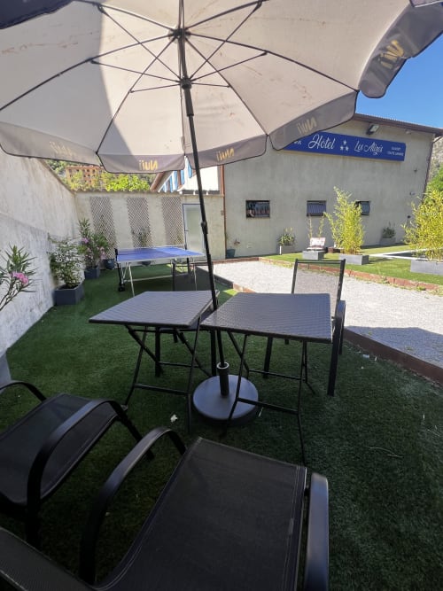 Outdoor patio at Hôtel les Alizés in Puget-Théniers with umbrellas, dining tables, ping pong table and green lawn