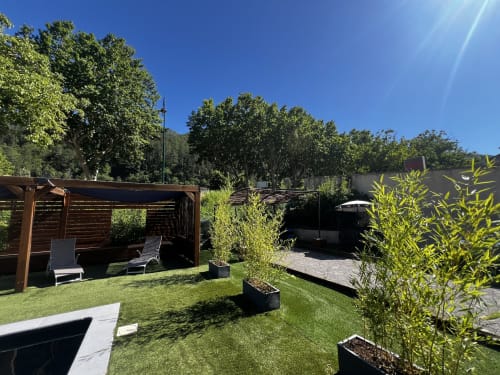 Sunny backyard garden at Hôtel les Alizés in Puget-Théniers with lounge seating, wooden pergola, and manicured lawn