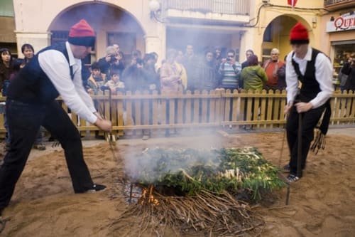 Celebración tradicional de salto de fuego en Hostal Grau en Tarragona, España con espectadores observando a actores en traje de época